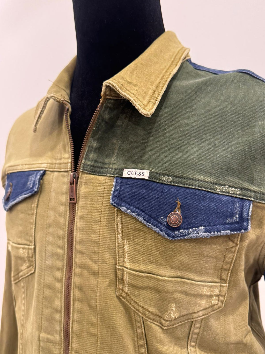 GUESS men's colorblocked denim jacket featuring olive and dark blue paneled sections with a front zipper closure.