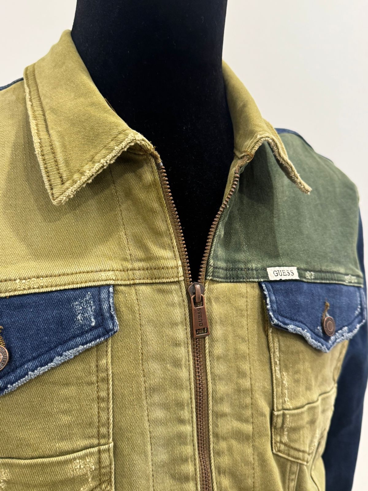 GUESS men's colorblocked denim jacket featuring olive and dark blue paneled sections with a front zipper closure.