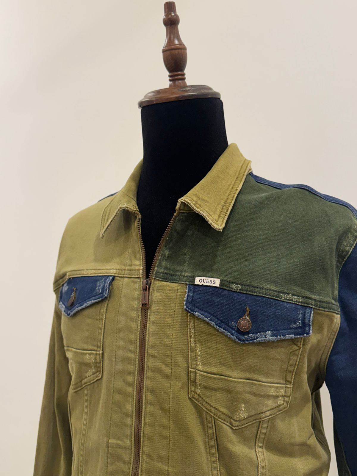 GUESS men's colorblocked denim jacket featuring olive and dark blue paneled sections with a front zipper closure.